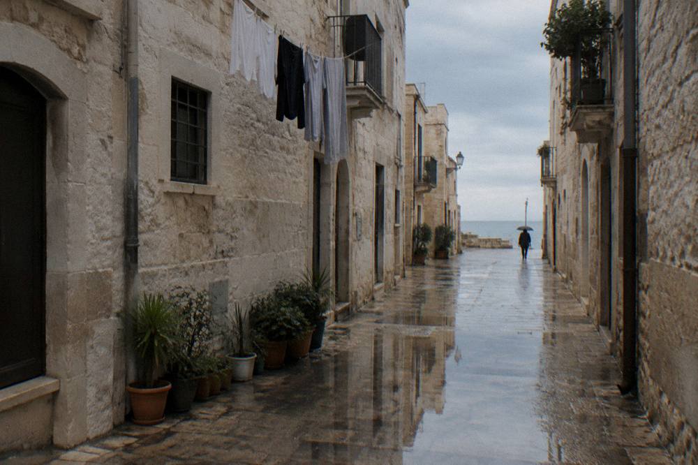 Wet limestone old town lane after rain with reflections in puddles and a distant person under an umbrella