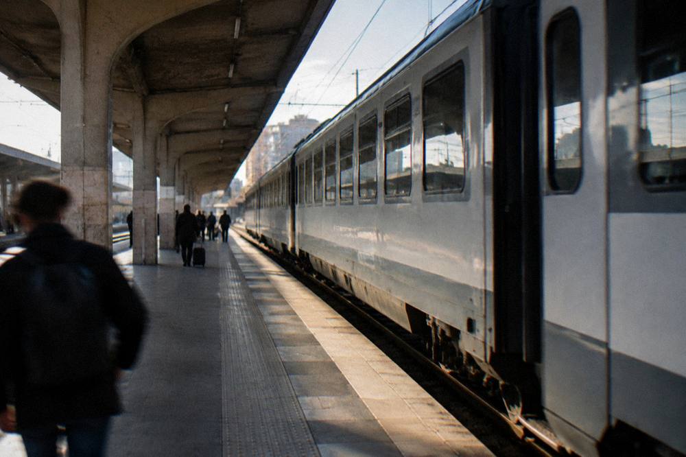 Regional train pulling into a station platform under a long canopy with a few distant waiting travellers