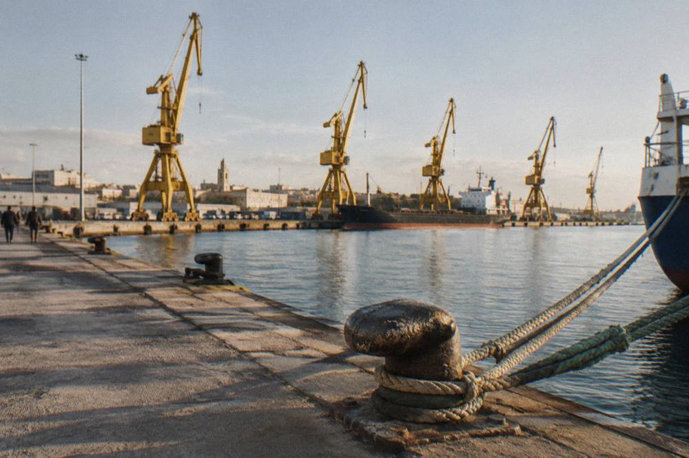 Row of harbour cranes behind a calm commercial dock with ropes and bollards in the foreground