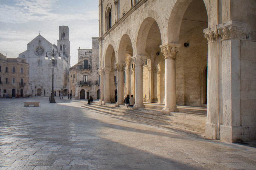 Loggia arches with long afternoon shadows and a few distant people sitting on the steps