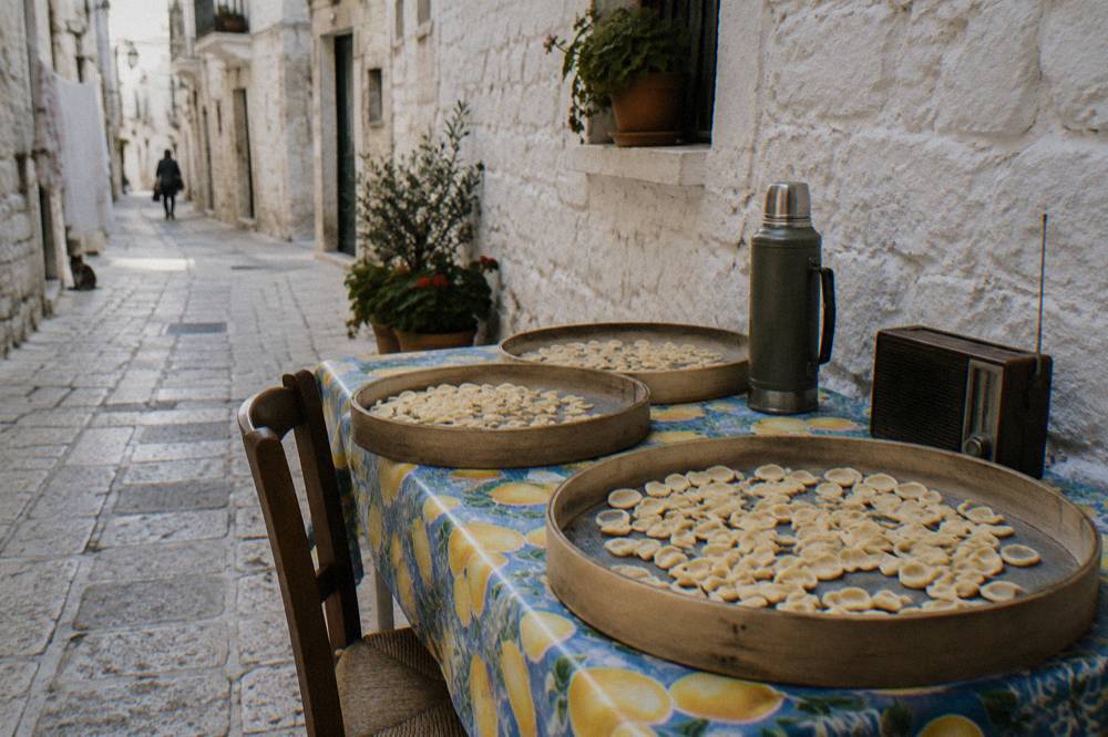 Lane-side table with sieves of drying orecchiette, a thermos and a radio against a whitewashed wall