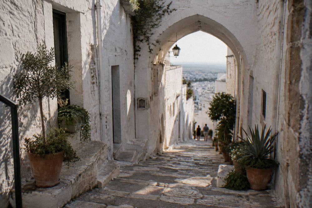 Steep whitewashed alley with stone steps, a pointed arch overhead and potted plants