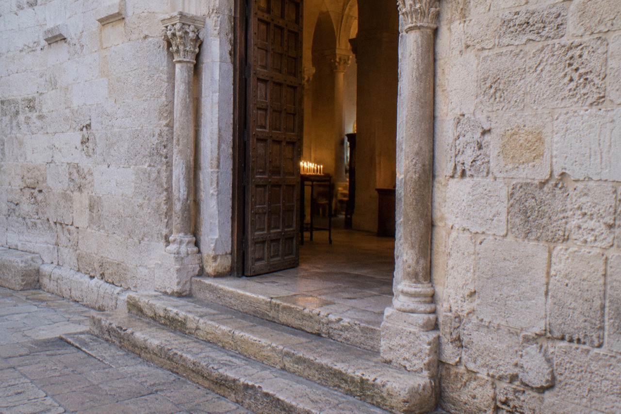 Side doorway of a Romanesque basilica with worn steps and a wooden door ajar on warm light