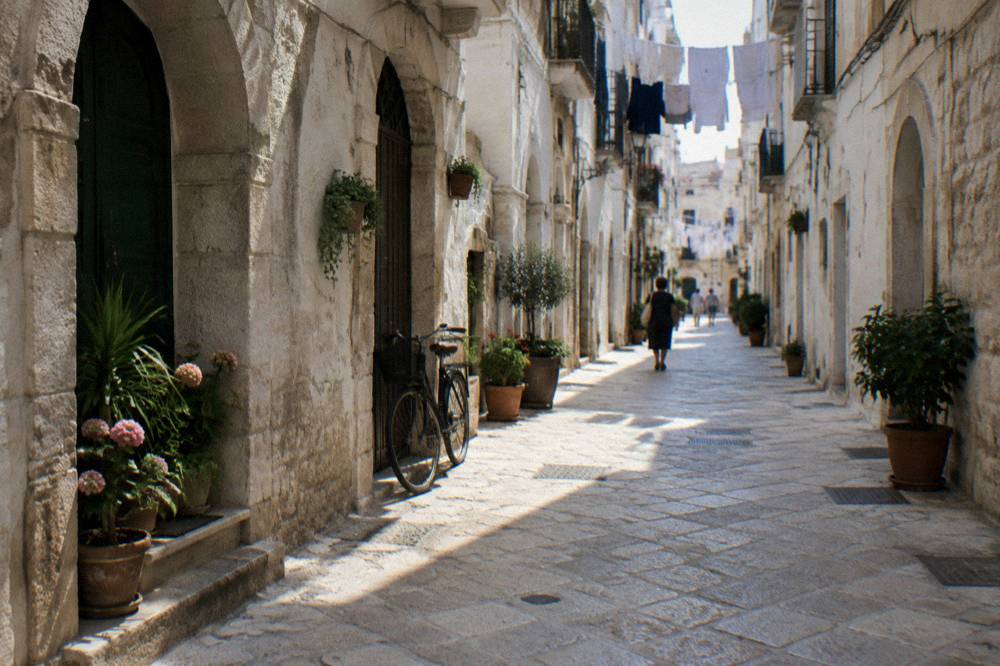 Narrow whitewashed old town lane with arched doorways, flower pots, washing overhead and a leaning bicycle in soft morning light