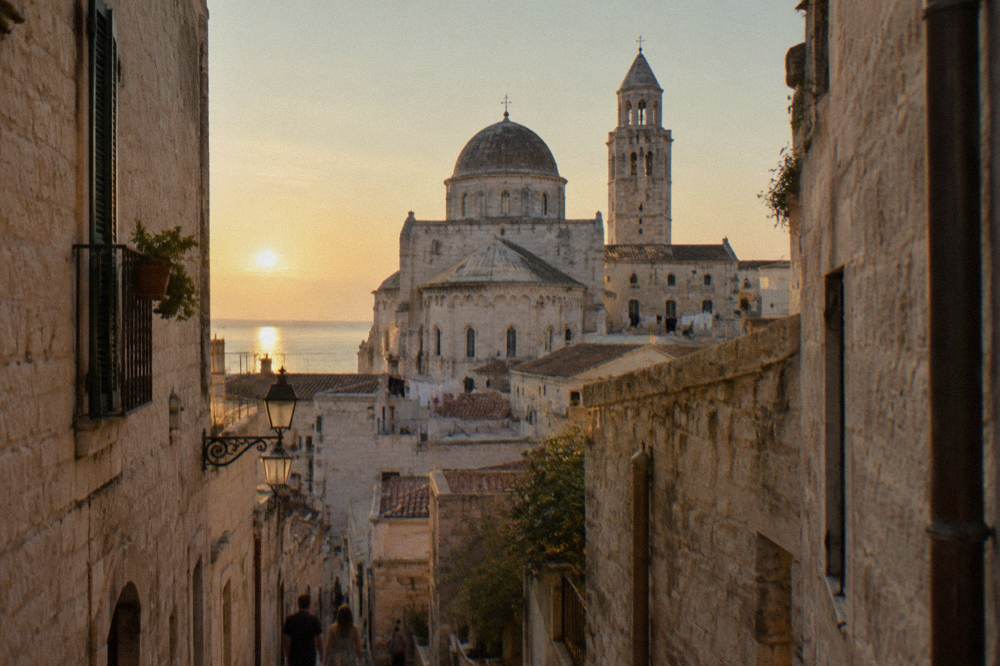 Cathedral dome and apse rising above terracotta rooftops at the end of a narrow old-town lane in afternoon light