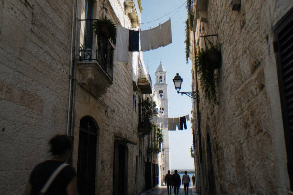 Looking up between close walls at a strip of blue sky crossed by washing lines and a bell tower
