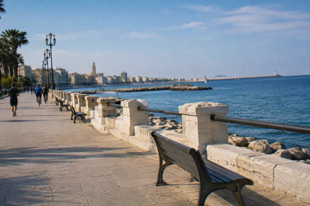 Wide paved seafront promenade with distant joggers and cyclists, benches and calm blue sea in late afternoon