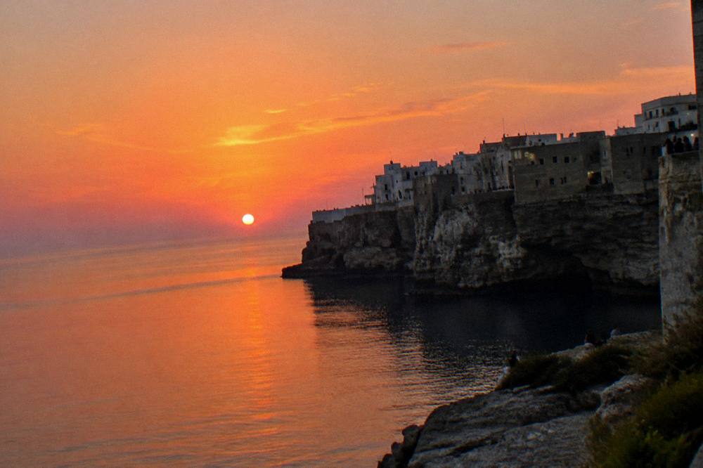 Cliff-top town in silhouette against a pink and orange sunset over a calm sea