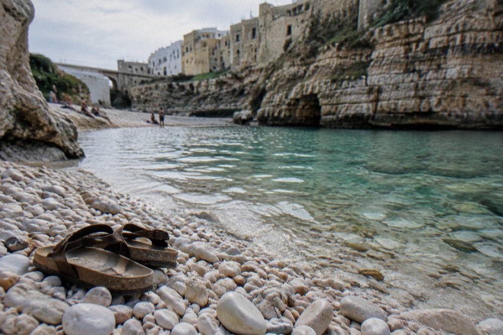 White pebbles and clear shallow water at the edge of a cove with a pair of sandals left on the stones
