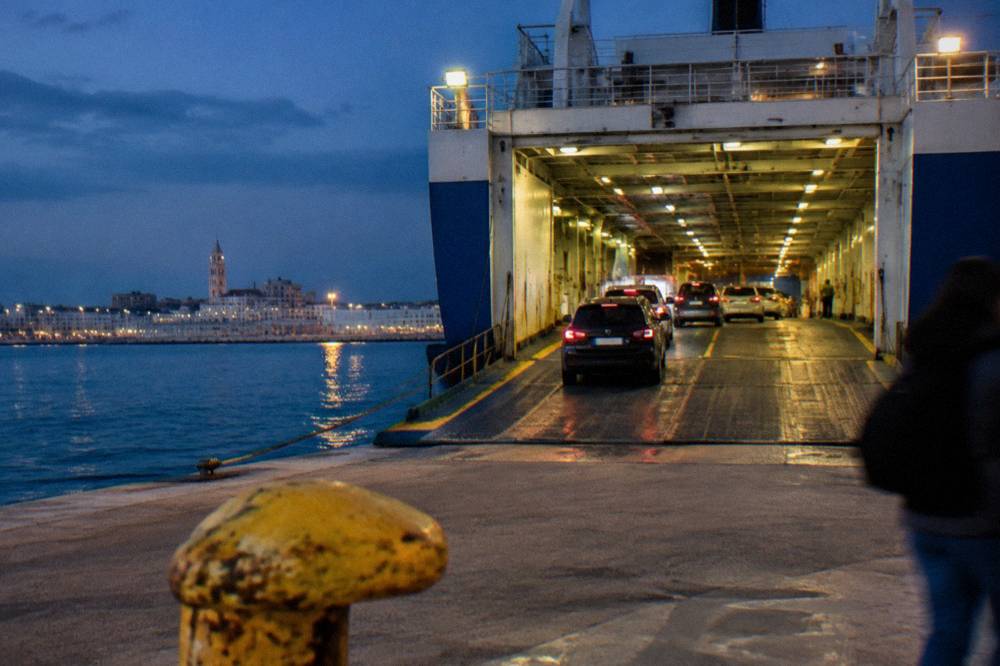 Ferry vehicle deck seen from the quay with rows of cars driving in under floodlights at evening