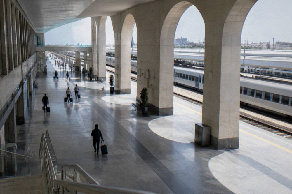 Large pale railway station with a long concourse, distant travellers with suitcases and plain trains at the platforms