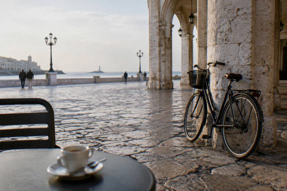 Worn limestone paving beside loggia arches with a leaning bicycle and an espresso cup on a small round table
