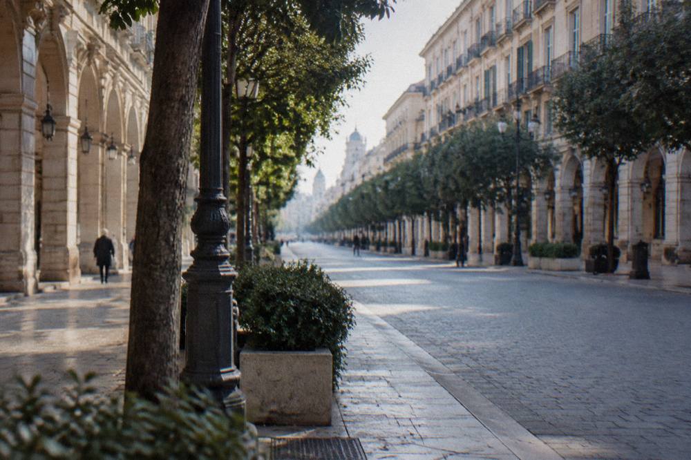 Long straight tree-lined boulevard of neoclassical buildings with arcaded ground floors