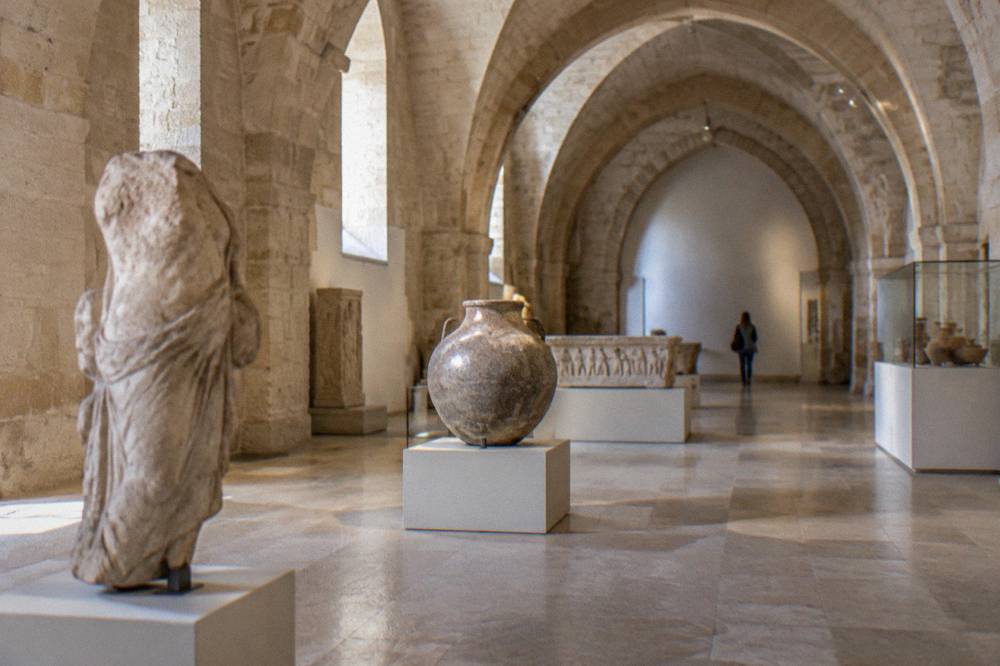Vaulted stone hall with archaeological finds on plain plinths in soft light