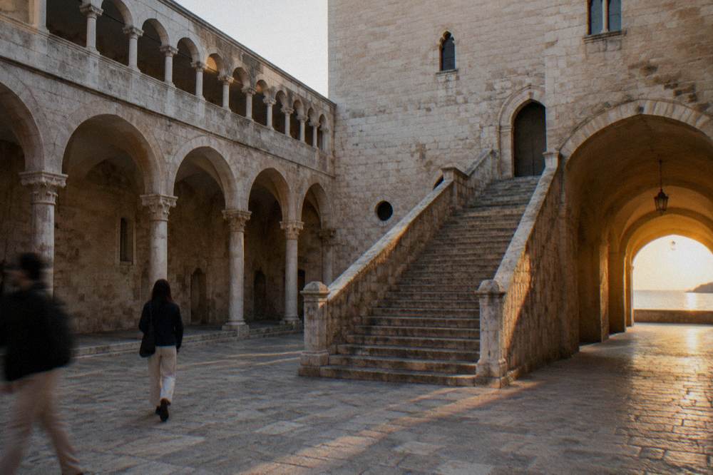 Inner courtyard of a medieval castle with a pale stone arcade, a broad staircase and a vaulted passage