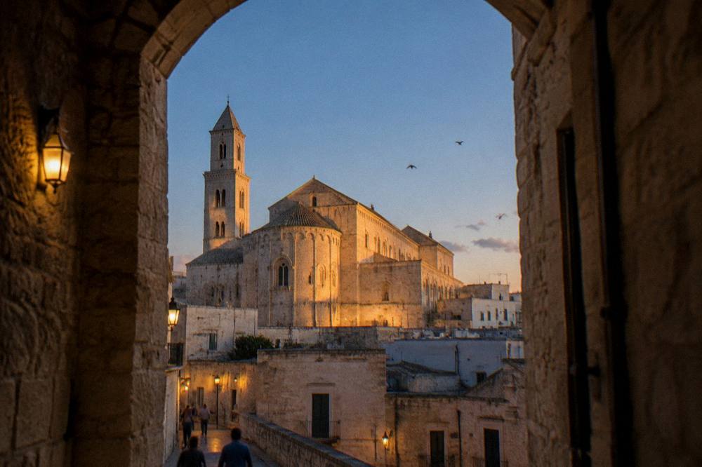 Basilica apse and walls glowing in low evening light above old town rooftops with swifts in the sky