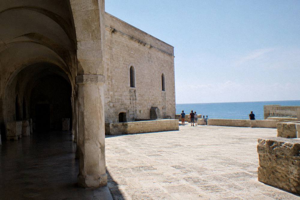 Low pale stone former monastery beside the sea with arched windows and a bare stone terrace