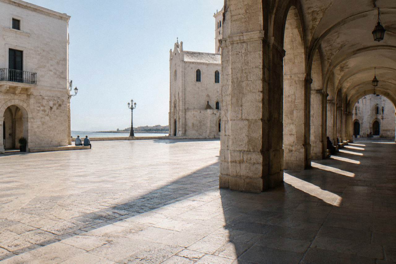 Loggia arches with long afternoon shadows and a few distant people sitting on the steps
