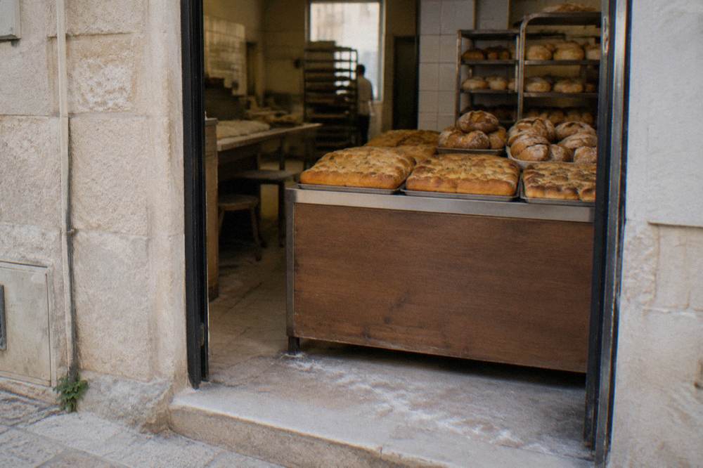 Neighbourhood bakery doorway with trays of golden focaccia and round loaves seen from the street