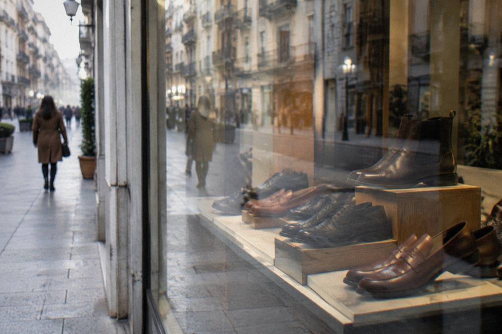 Shop window with leather shoes behind glass reflecting the street and a blurred passer-by