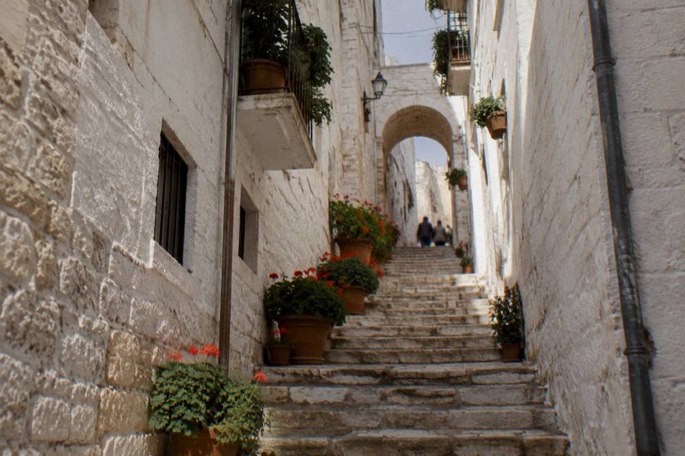 Narrow lane with a steep stone staircase climbing between whitewashed walls to a small arch with potted geraniums