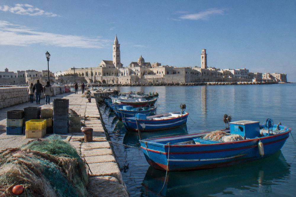 Old harbour pier with small wooden fishing boats, crates and nets and the pale old town skyline with two towers behind