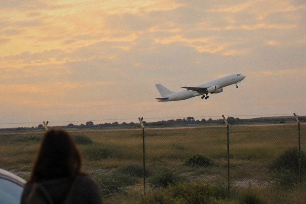 Plane taking off low over scrubby fields beyond a perimeter fence at golden hour