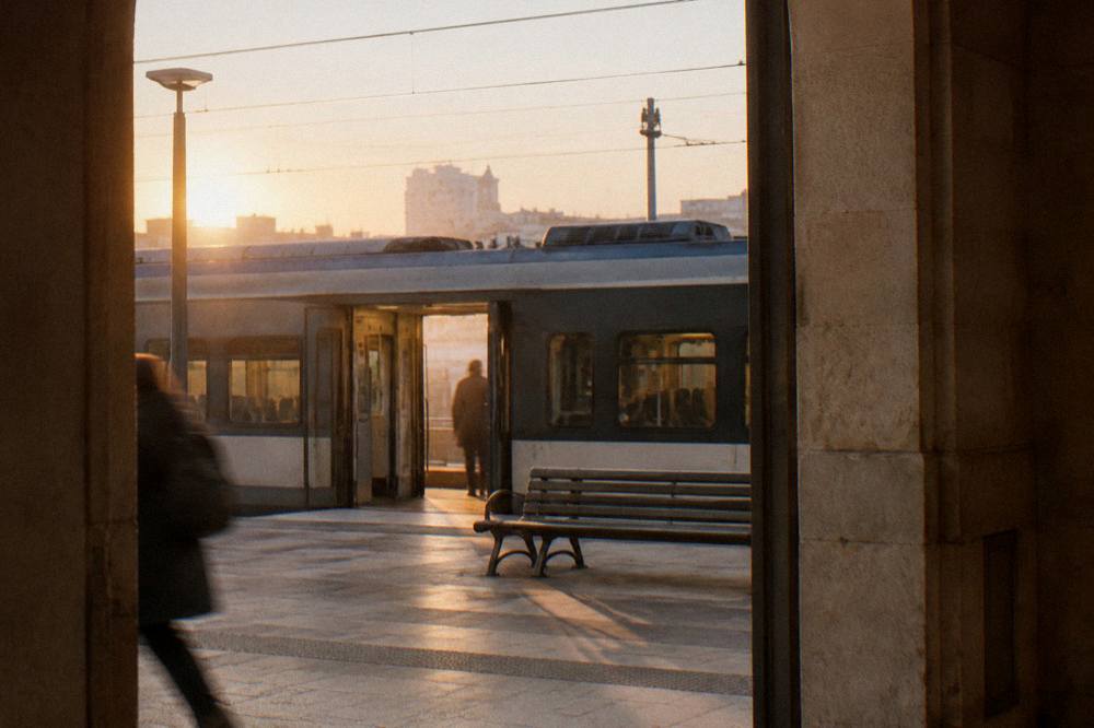 Railway platform at golden hour with a plain regional train waiting with open doors and an empty bench
