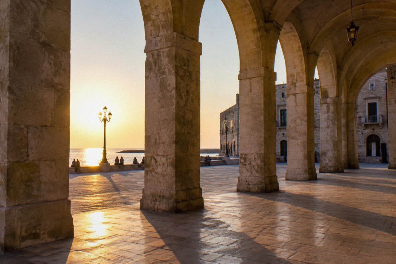 Loggia arches with long afternoon shadows and a few distant people sitting on the steps