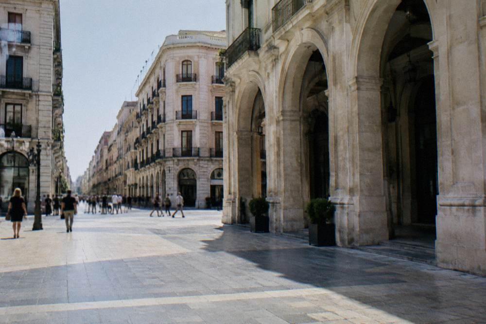 Shoppers far off crossing the paved intersection of a pedestrian street between tall facades