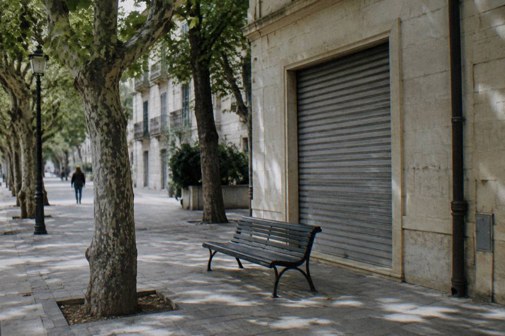 Shaded corner of a district with a cream stone shopfront, a bench and dappled light
