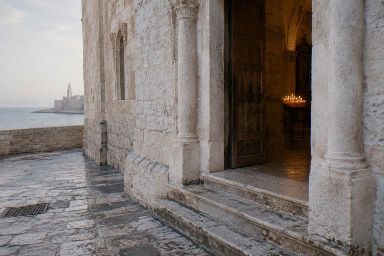 Side doorway of a Romanesque basilica with worn steps and a wooden door ajar on warm light