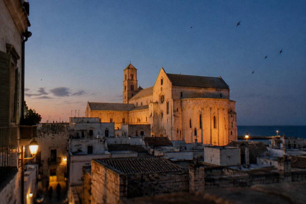 Basilica apse and walls glowing in low evening light above old town rooftops with swifts in the sky
