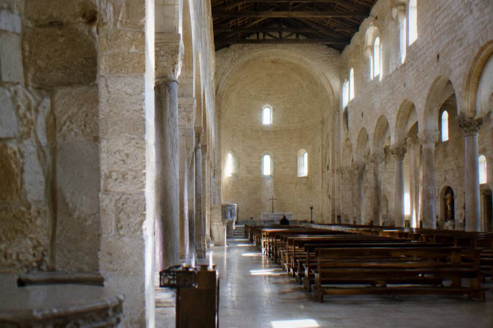 Bare stone cathedral interior with round arches, a high apse and shafts of light from small windows