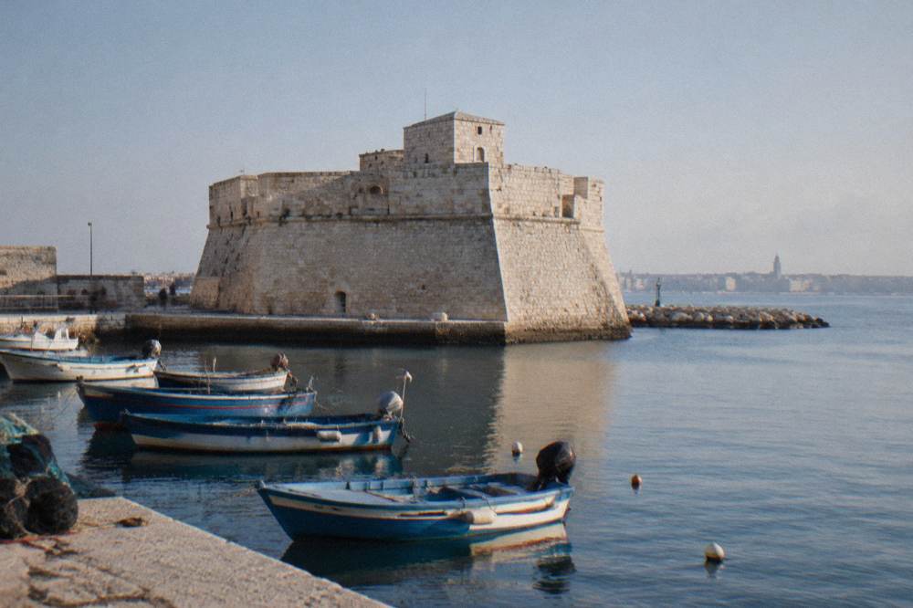 Squat pale limestone fort with thick sloping walls at the edge of the old harbour with small fishing boats moored in front