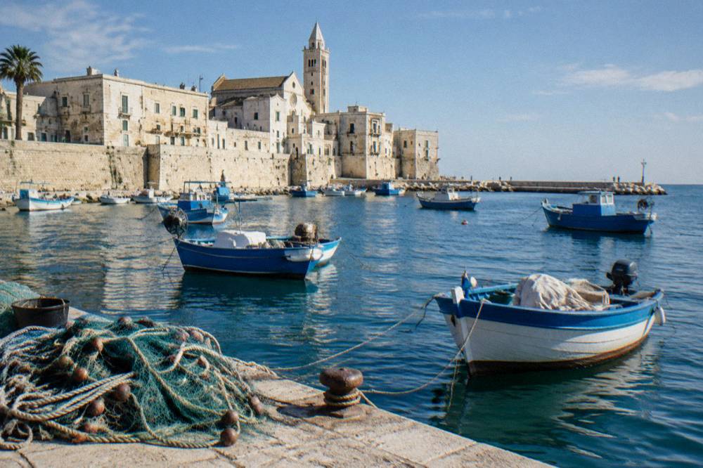 Small wooden fishing boats rocking at moorings with a net heap on the quay and pale old town walls behind
