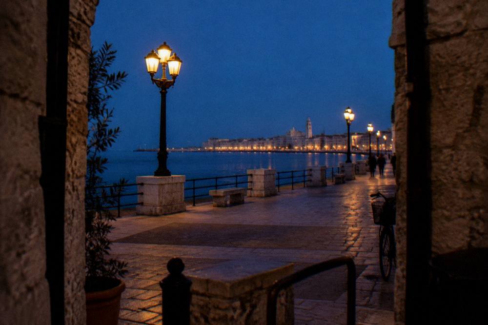 Seafront promenade at blue hour with lit street lamps and the lights of the old town across the bay