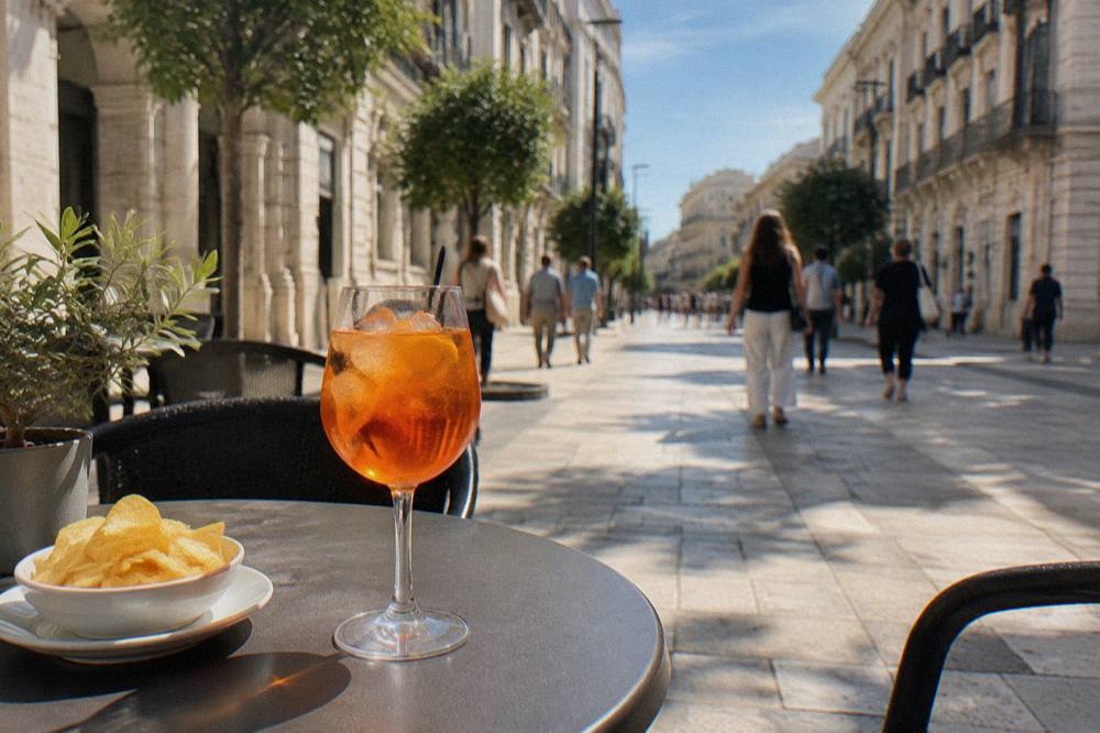 Pavement cafe table on a pedestrian street with an orange spritz and a small plate of crisps, passers-by blurred