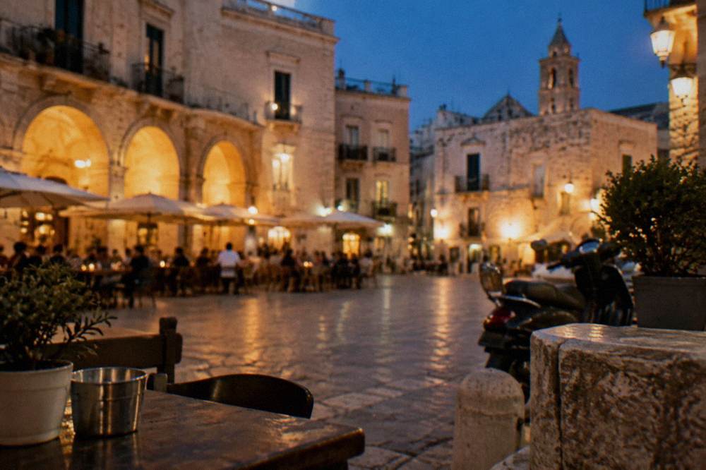 Evening piazza with warm light on cream walls, out-of-focus diners at tables and glowing market arches