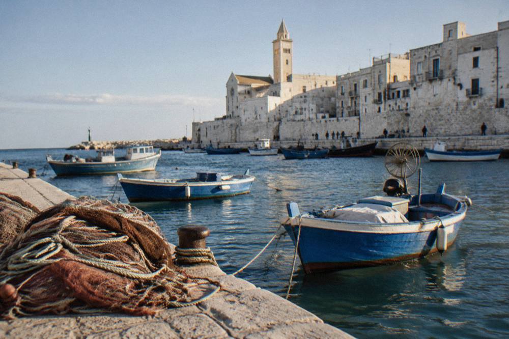 Small wooden fishing boats rocking at moorings with a net heap on the quay and pale old town walls behind