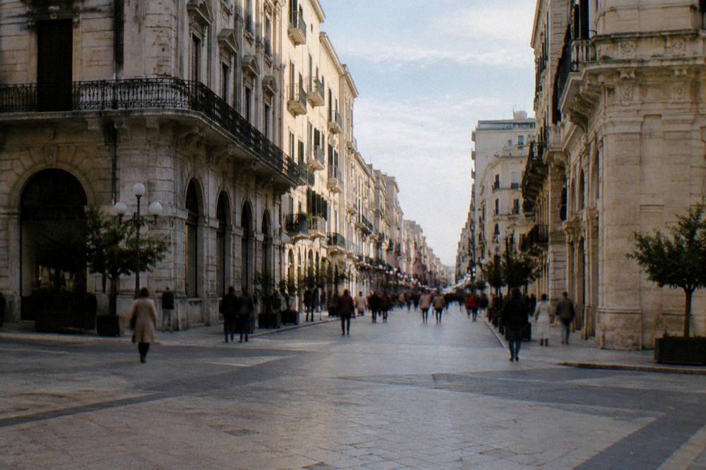 Shoppers far off crossing the paved intersection of a pedestrian street between tall facades