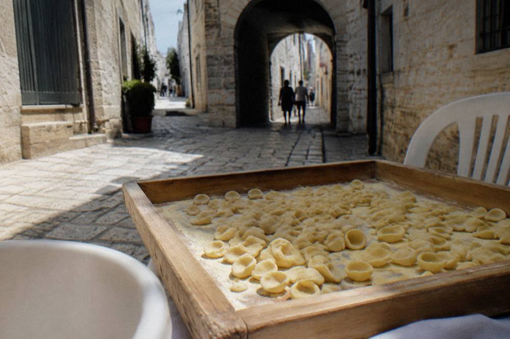 Tray of small ear-shaped orecchiette dusted with semolina on a wooden table beside a plastic chair