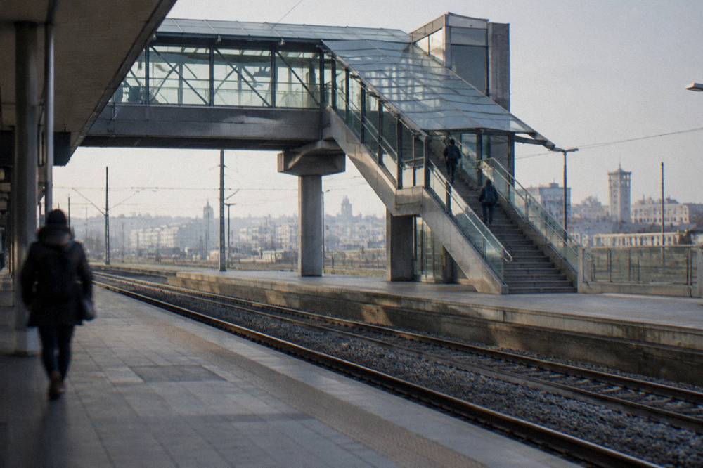 Station footbridge with stairs and a glass roof and a distant traveller with a rucksack