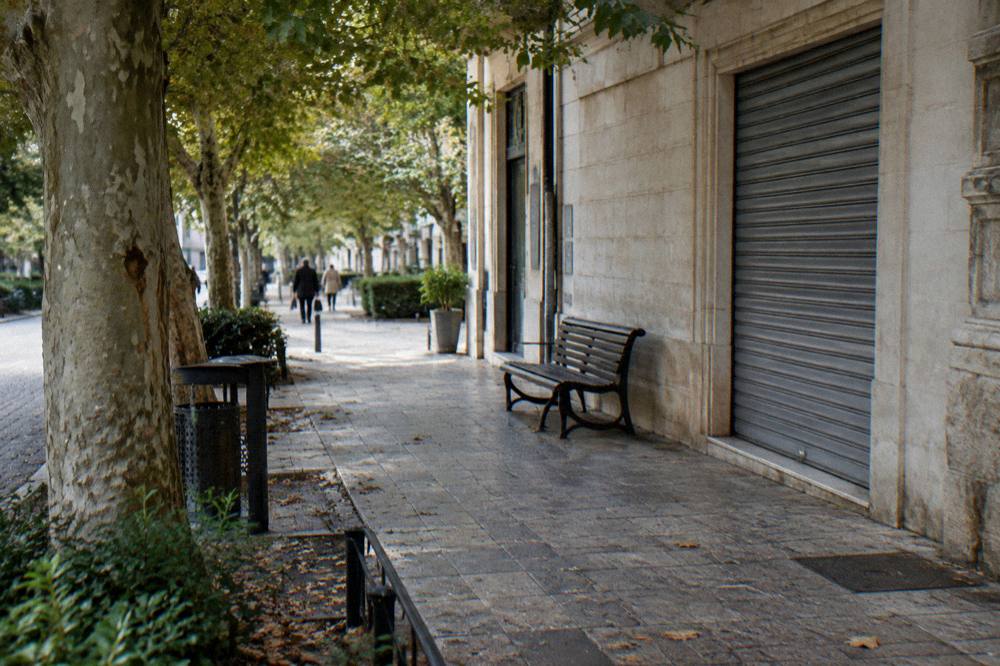 Shaded corner of a district with a cream stone shopfront, a bench and dappled light