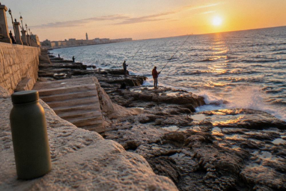 Stone steps down to flat limestone rocks below a sea wall with distant anglers fishing and light sea spray