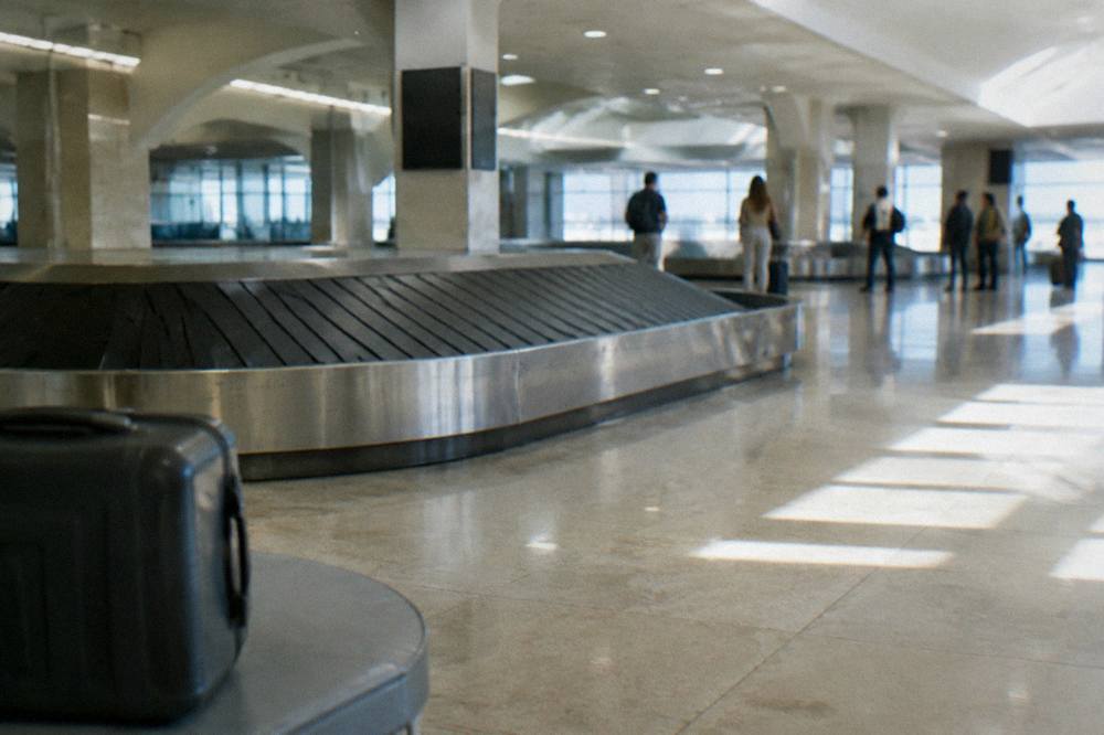 Baggage reclaim hall with an empty belt curving through and a few travellers watching far off