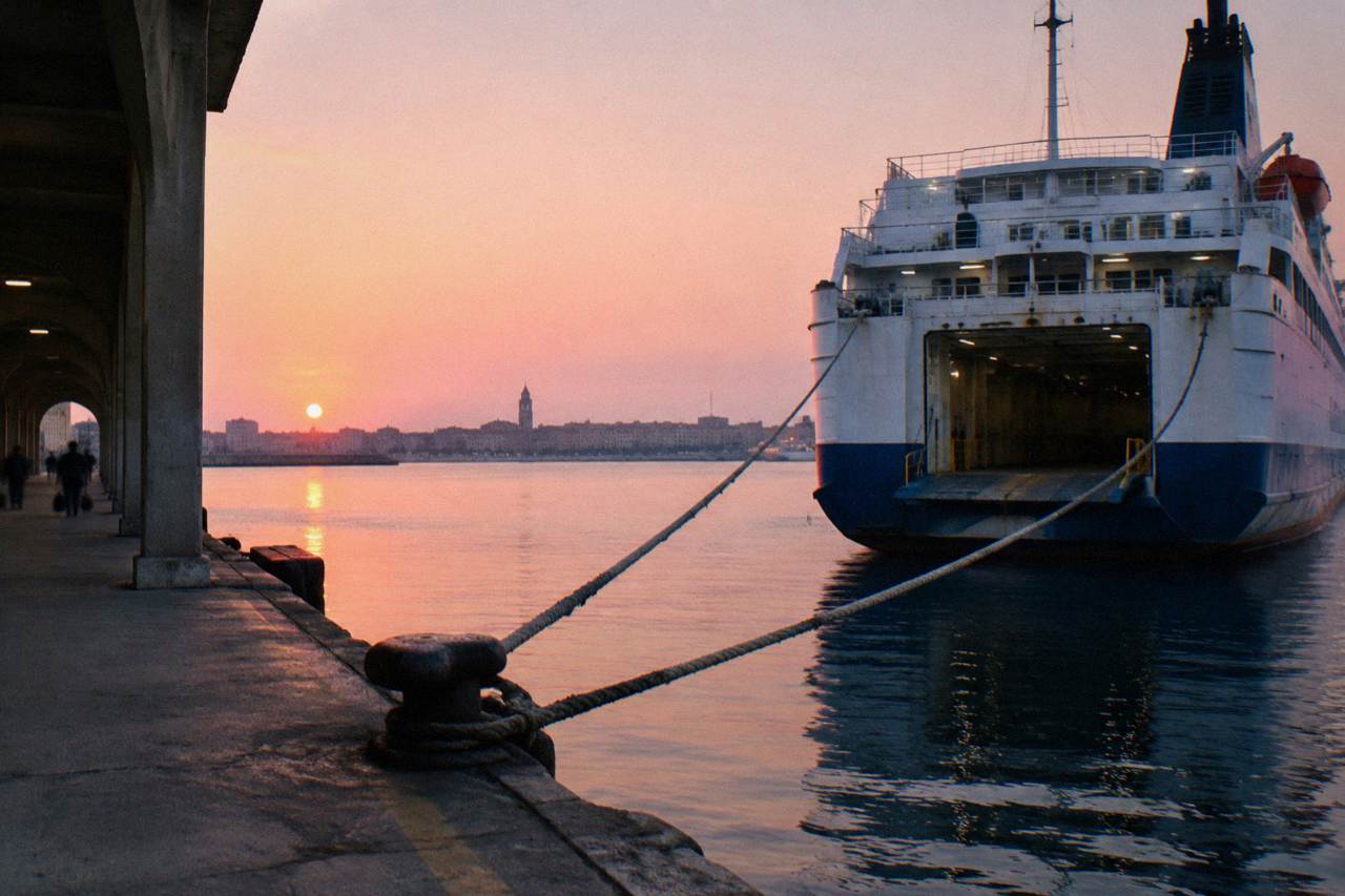 Stern of a ferry at a quay at sunrise with a pink sky, taut mooring ropes and still water