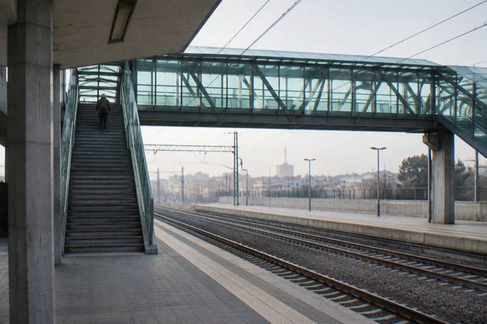 Station footbridge with stairs and a glass roof and a distant traveller with a rucksack