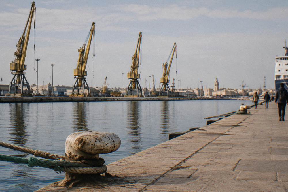 Row of harbour cranes behind a calm commercial dock with ropes and bollards in the foreground