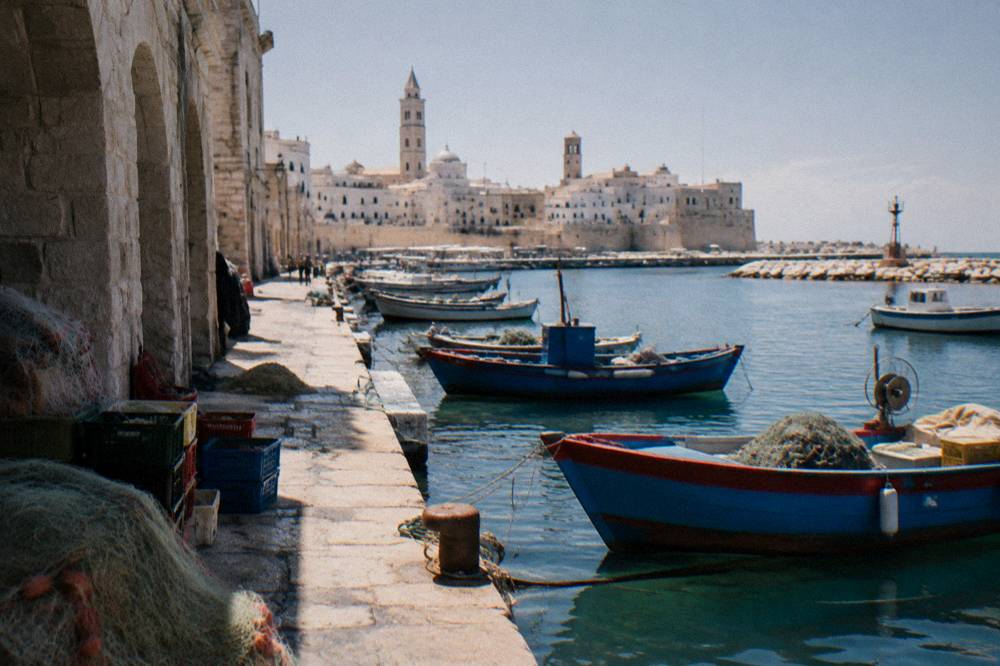 Old harbour pier with small wooden fishing boats, crates and nets and the pale old town skyline with two towers behind
